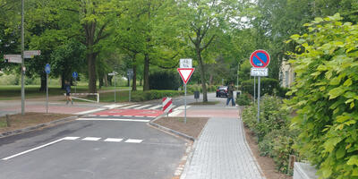 Eine auf eine Spur verengte Straße. Darüber verläuft ein rot markierter Radweg; Parallel dahinter ein Zebrastreifen.